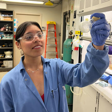 Student in chemistry lab holds up a beaker and looks at contents.