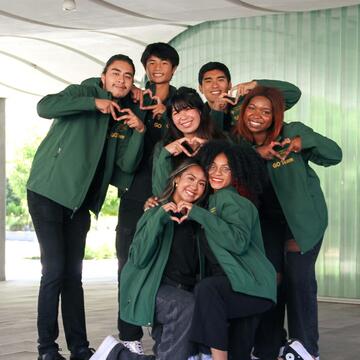 Students in green jackets making heart signs with their hands