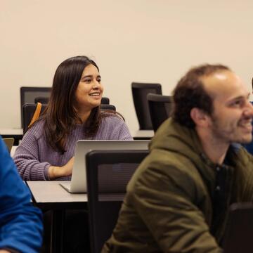 Students in class smiling and sitting in front of laptops