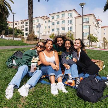 Five students sitting on grass smiling