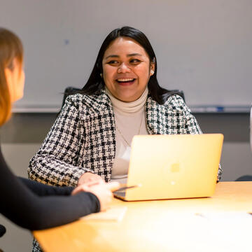 Three students chatting and smiling, working on laptops
