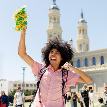 Student cheers with a pom pom in hand in front of the church.