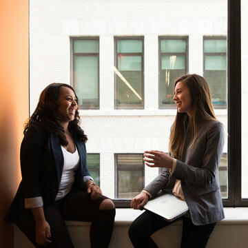 Two women talking in a room in front of a window