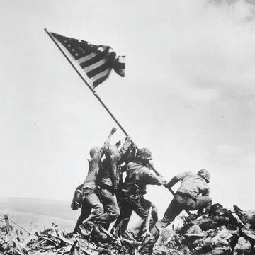 World War 2 soldiers lifting American flag.