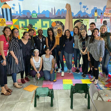 Migration studies students posing in a classroom with mural behind