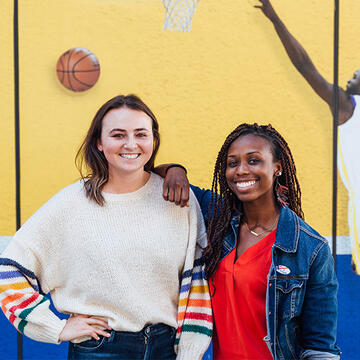 Two sport management students posing in front of basketball mural