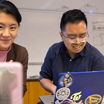 Student and professor looking at laptops and smiling