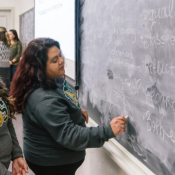 student writes on chalkboard