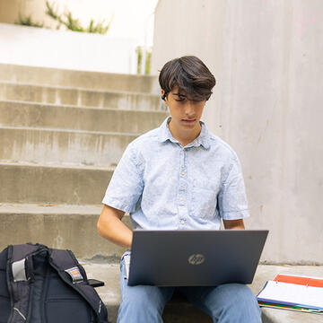 student uses laptop outside on campus steps