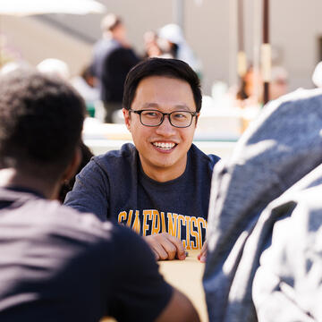 Student with glasses and a USF crewneck chatting with peers