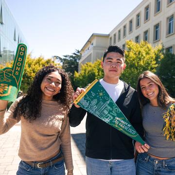 Three students posing on campus waving USF merch