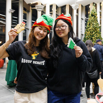Two students holding cookies in front of a christmas tree