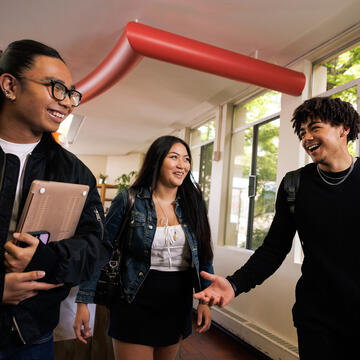 Three students talk while walking on campus.