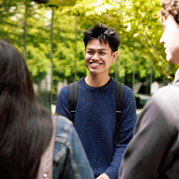 student wearing backpack smiles at others outside
