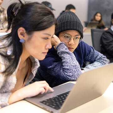 Two students huddle over a computer