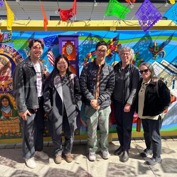 group of students stand in front of colorful mural