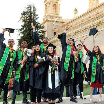Several students celebrate graduation with a cheer and throwing hats in the air