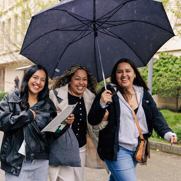 three students holding umbrella while walking on campus