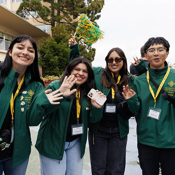 usf students wearing green wave at camera during an event on campus