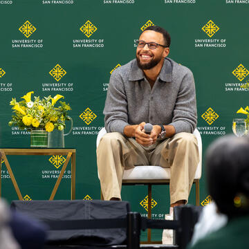 Steph Curry sits on stage and smiles at crowd at the Silk Speaker Series event