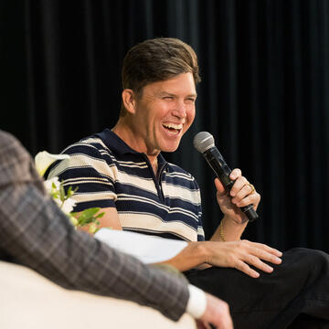 Colin Jost laughing into a microphone at the Silk Speaker Series