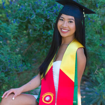 Trinna Hovan seated in front of flowers with a graduation cap and sash