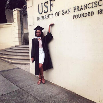 Sydney Powell '17 in cap and gown next to the University of San Francisco sign at 2130 Fulton Street