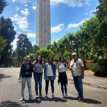 Five individuals stand on a path in front of a bell tower.