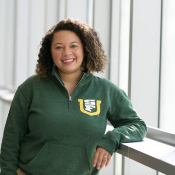 Student, leaning against wall, looks at camera.