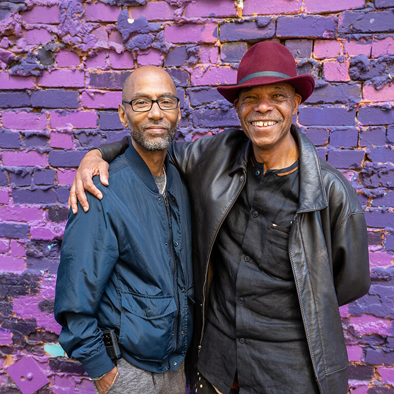 two people smiling together outside next to a purple wall