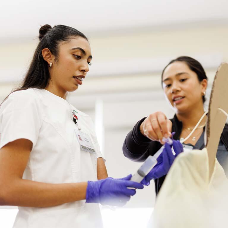 Student holding a syringe with professor instructing