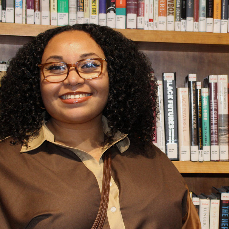 student smiles in front of bookshelf at a public library