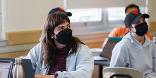 Students with laptops look to the right while listening