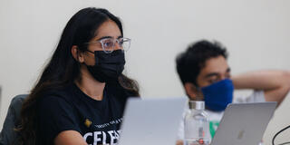 Student with a laptop and a water bottle next to it listens attentively