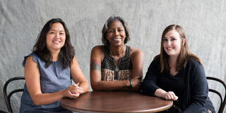 Three students sitting at a table smiling.