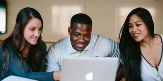 Three students study around a laptop.