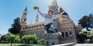 Student jumps in the air in front of St. Ignatius Church holding pom poms