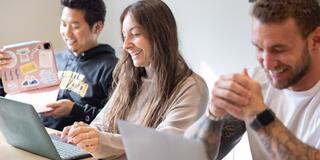 Three people sitting at a table with their laptops.