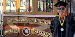 Image of a person in front of a trolley wearing their graduation regalia