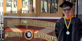 Image of a person in front of a trolley wearing their graduation regalia 