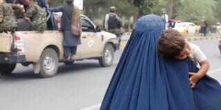 Woman with child walks by truck with armed men in Kabul
