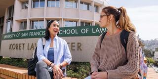 two students sitting by the usf school of law sign