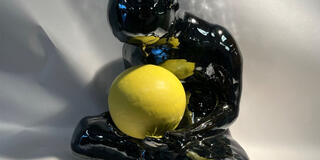 Glossy black sculpture of a seated figure holding a bright yellow sphere