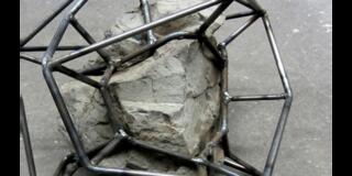 Metal geometric frame partially encasing a rough stone on a concrete surface.