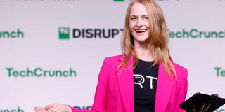 Courtney Jeffries in a black t-shirt and bright pink blazer, speaking to a crowd