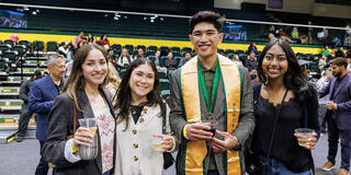 USF graduate smiling in regalia and posing with three friends