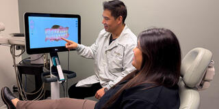 Person sitting in dentist office chair with the Dr. showing them a scan of their teeth on the computer screen