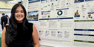student smiles in front of her research board at school of nursing and health professions event