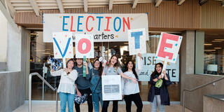 Students holding signs and talking into bullhorns, encouraging others to vote.