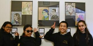 Students stand in front of art drawings pointing